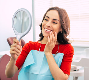 woman admiring new dental veneers in mirror and dentists office